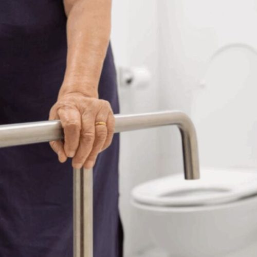 Pessoa idosa usando uma barra de apoio de metal em um banheiro com acessibilidade, garantindo segurança e conforto.